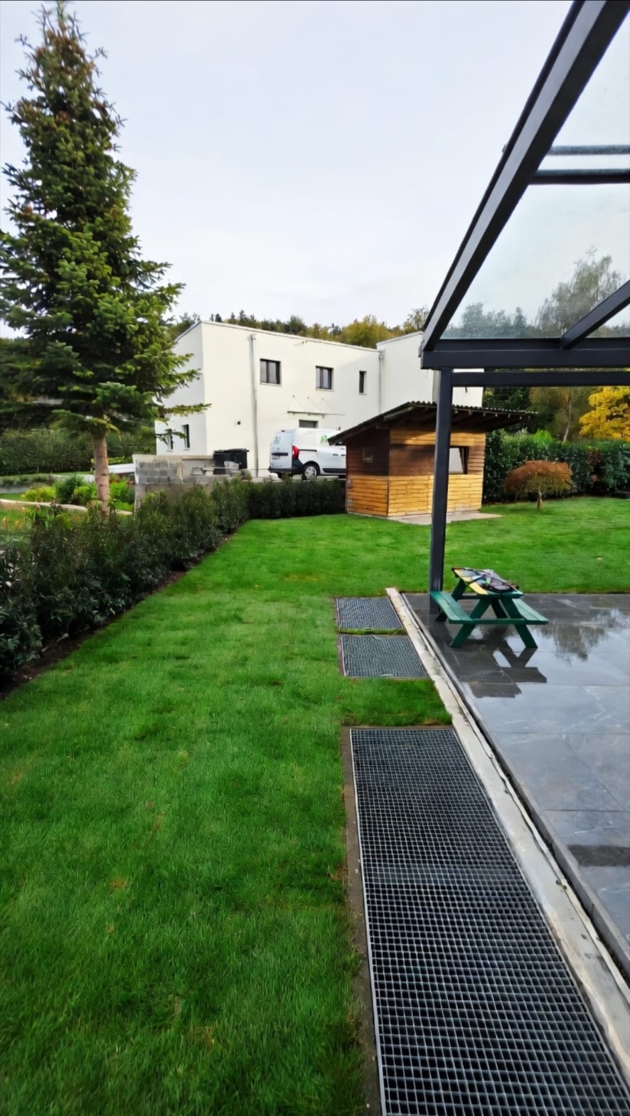 Rasenfläche mit Hecke, Gartenhaus und überdachtem Plattensitzplatz