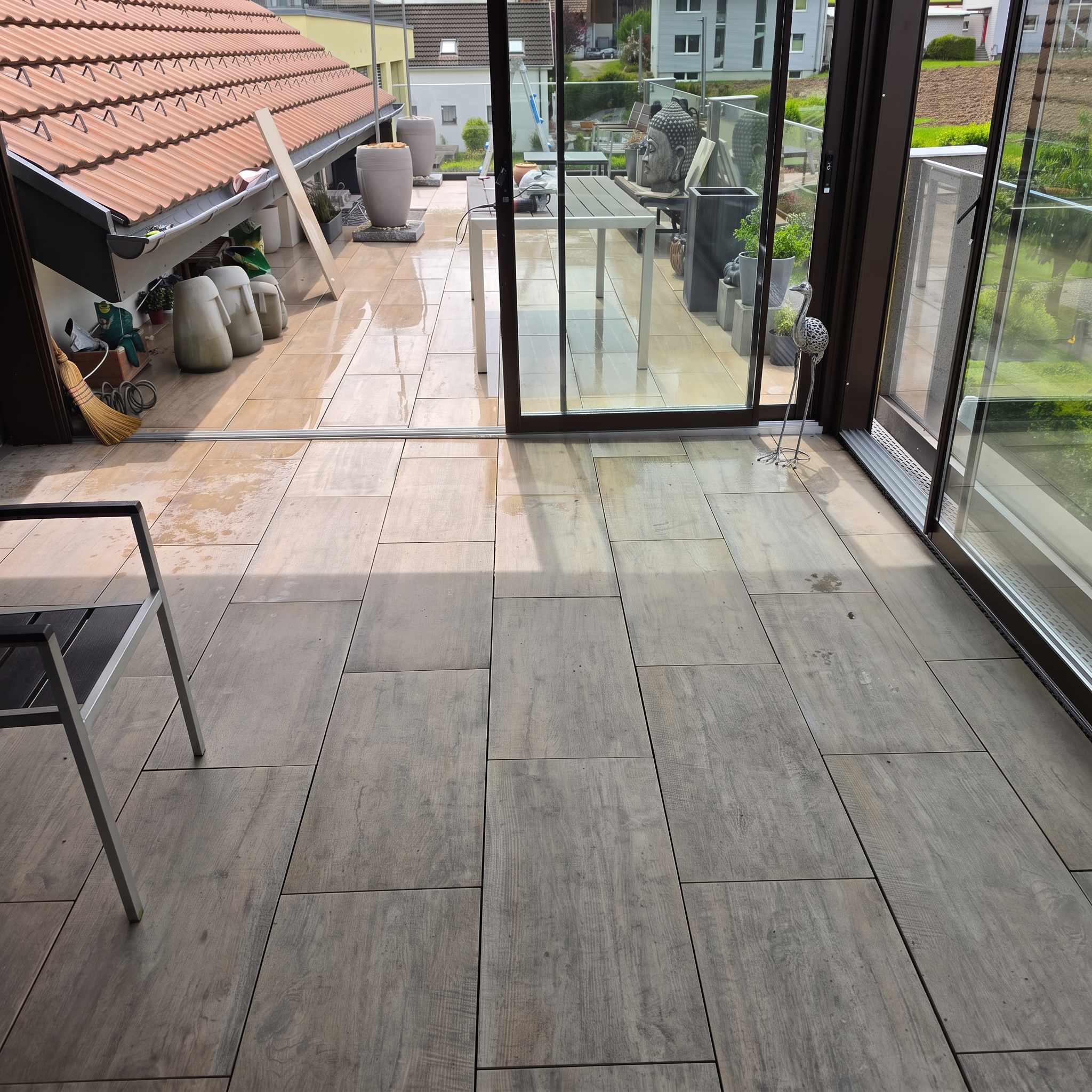 Überdachte Terrasse mit Holzoptik-Platten, Glas-Schiebetüren und Blick in den Garten