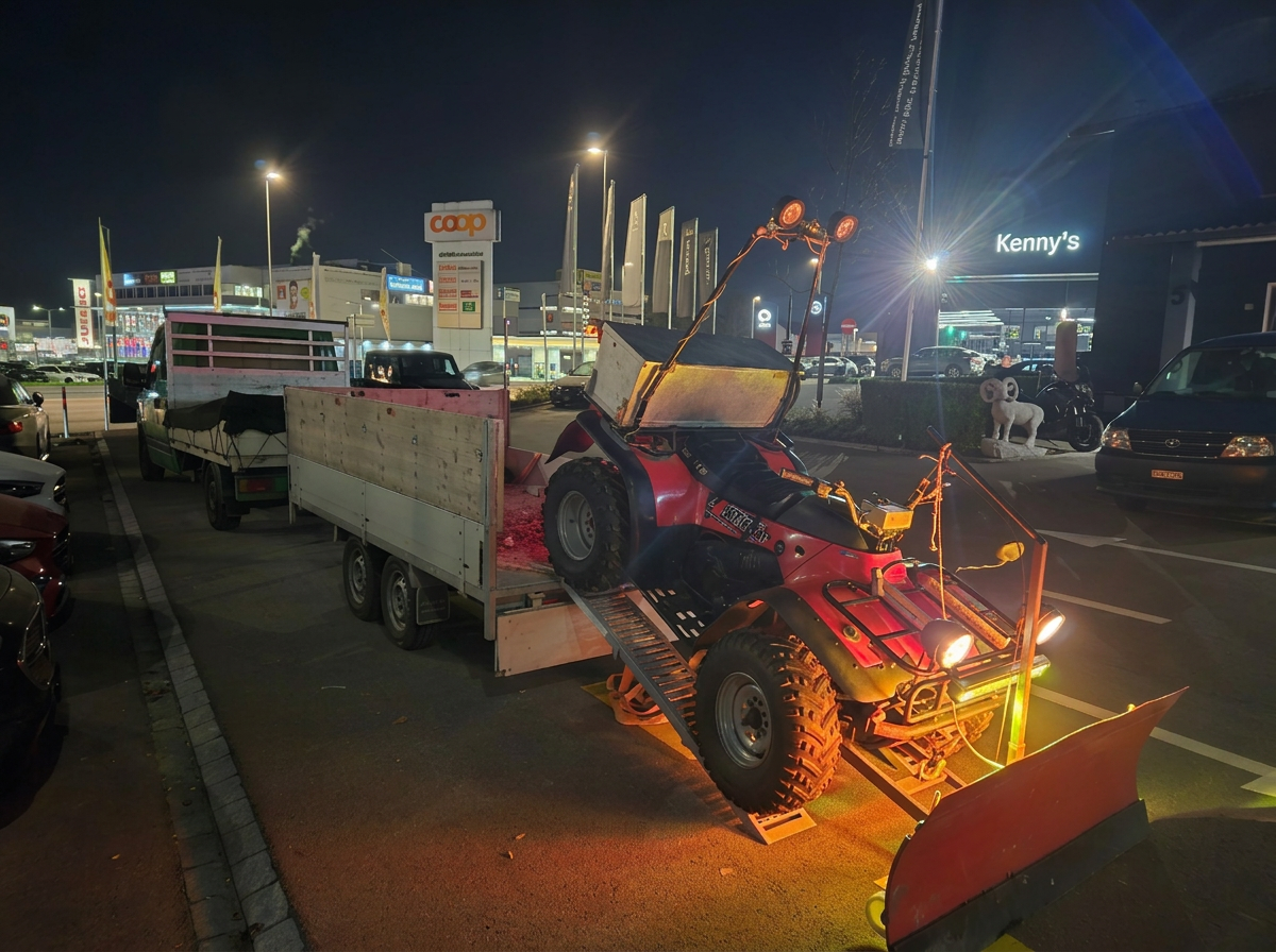 Quad mit Schneepflug wird bei Nacht auf einem Anhänger verladen